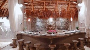 A restaurant with a thatched roof, a central bar area with stools, and a stone wall backdrop. - Villa Kassondra del Mar (Acajutla)