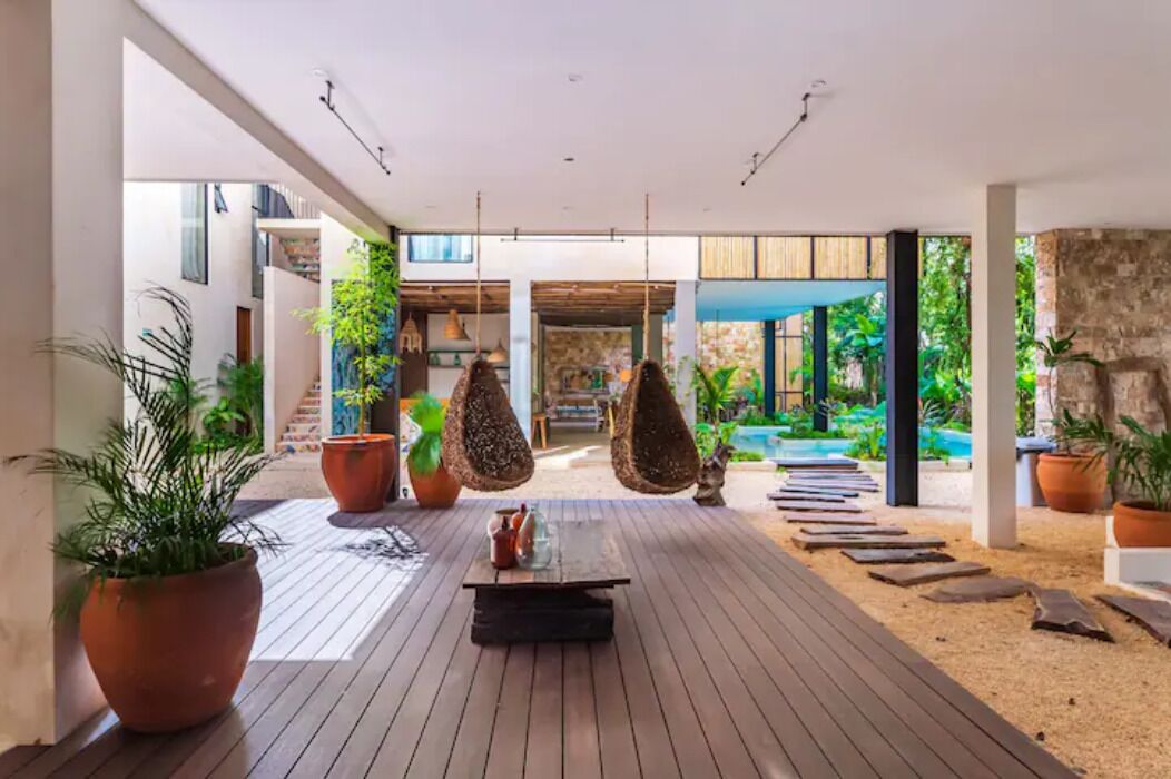 A modern outdoor lounge area with a wooden deck, hanging chairs, and potted plants.