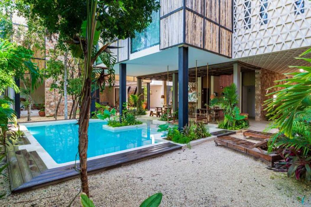 A pool area with a wooden deck, surrounded by lush greenery and a stone wall.