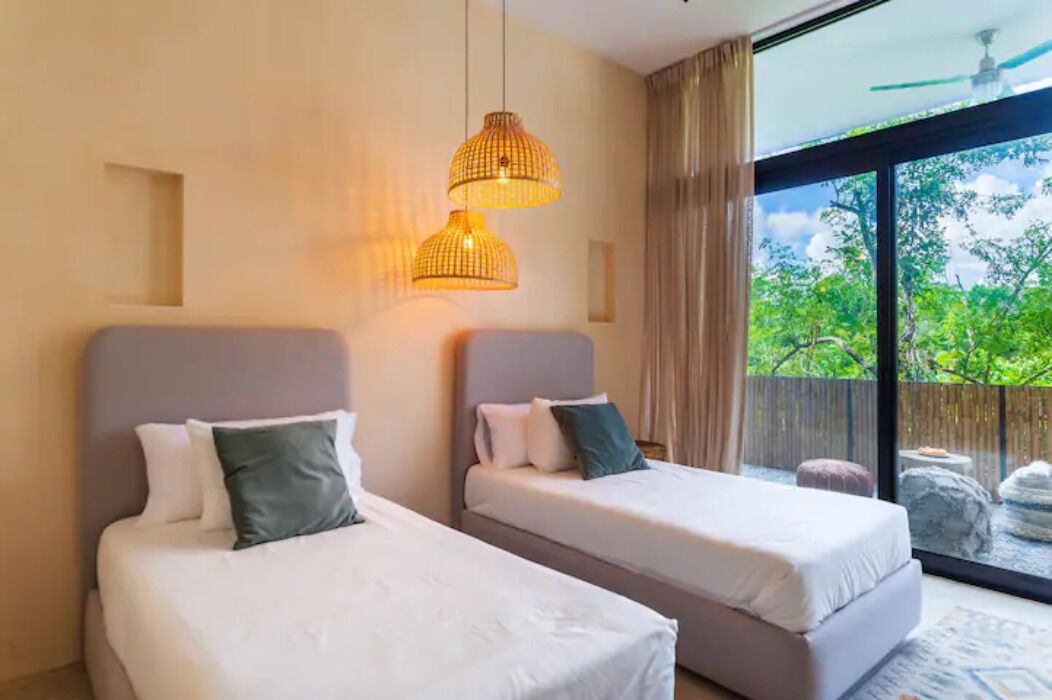 Une chambre d’hôtel avec deux lits, une grande fenêtre donnant sur un paysage verdoyant et un ventilateur de plafond.