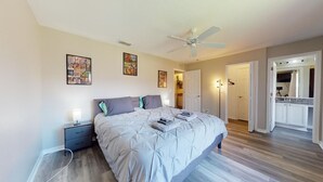 A bedroom with a bed, bedside tables, a ceiling fan, and a door leading to a bathroom. - Themed, 4 Bed, 3bth, Next To Pool, Water Slides, Walk To Oldtown, 6 to Disney. (Kissimmee)