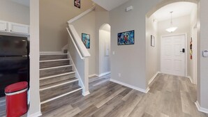 A modern interior with a wooden staircase, a kitchen area, and a hallway with artwork. - Themed, 4 Bed, 3bth, Next To Pool, Water Slides, Walk To Oldtown, 6 to Disney. (Kissimmee)