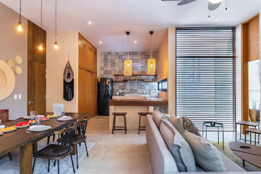 Une cuisine moderne dotée d’un îlot central, de luminaires suspendus et d’un coin repas avec un canapé et des chaises.