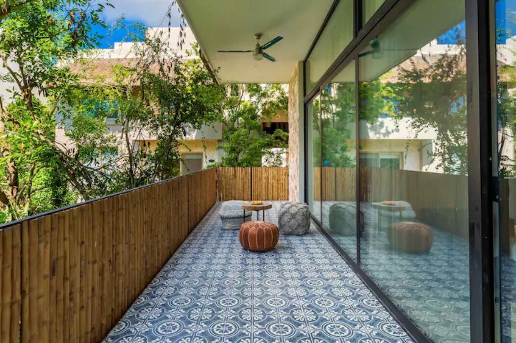 A balcony with patterned flooring, wooden railings, and a seating area with ottomans.