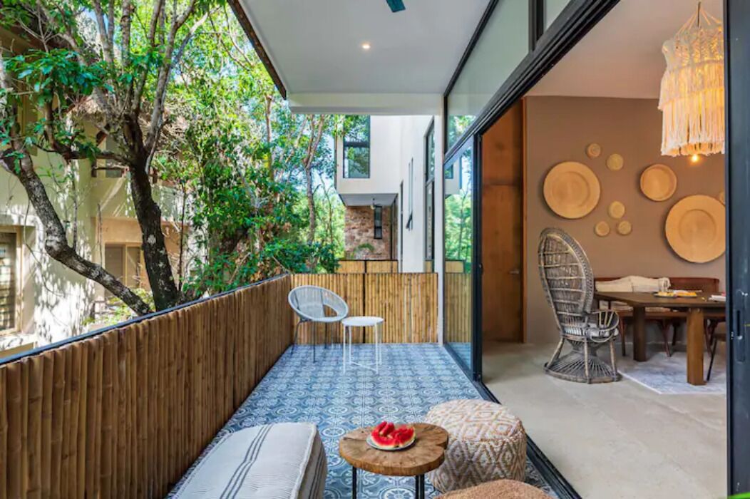 A modern outdoor seating area with a view of a tree-lined courtyard, a dining area with a wooden table and chairs, and a patterned floor.