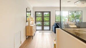 Une chambre d’hôtel moderne avec une grande fenêtre, un plancher en bois, un canapé et une table de chevet avec une lampe.