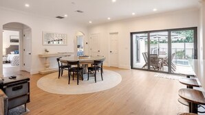 Un vaste espace dédié à la salle à manger, avec une table ronde et des chaises, une grande fenêtre donnant sur une piscine et du mobilier d’extérieur, ainsi qu’une porte-fenêtre coulissante qui mène à un balcon.