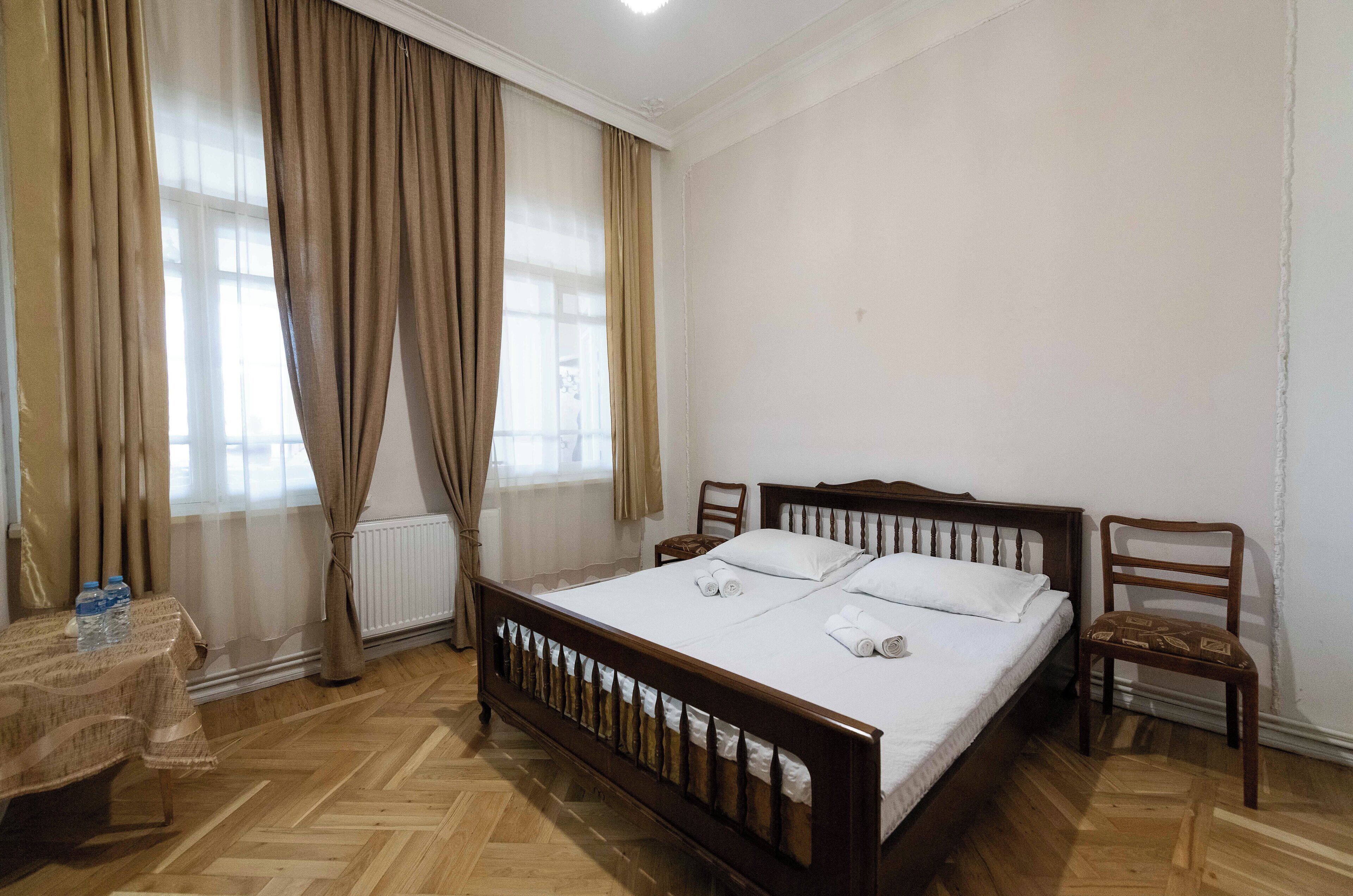 Un dormitorio con una cama de madera, una mesita con una botella y una silla.