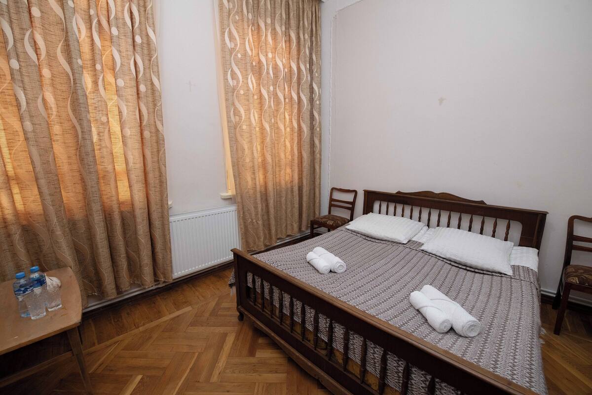 A neatly made bed with white linens and towels, a wooden headboard, and a wooden floor.