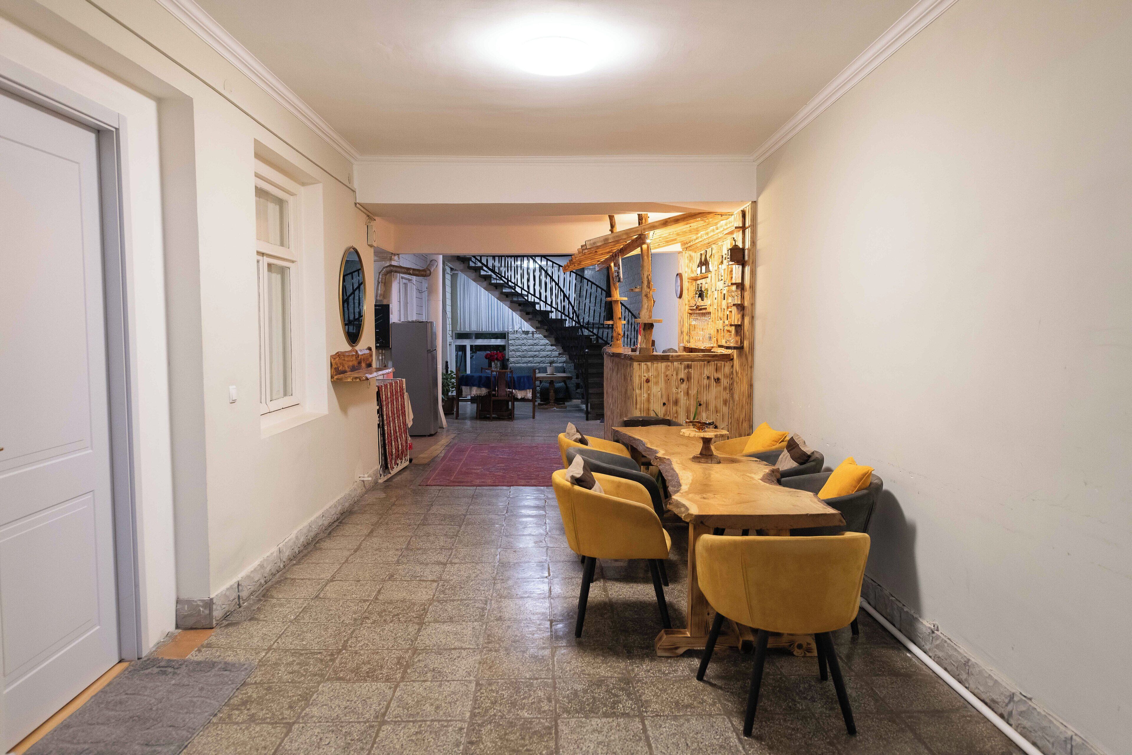 A hallway leading to a dining area with a wooden table and yellow chairs, a staircase, and a bar area with shelves.