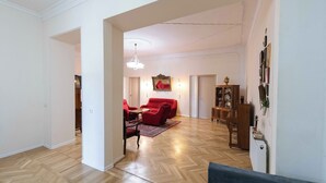 Amplia sala de estar con piso de parquet de madera, un juego de sofá rojo, una araña y una estantería.