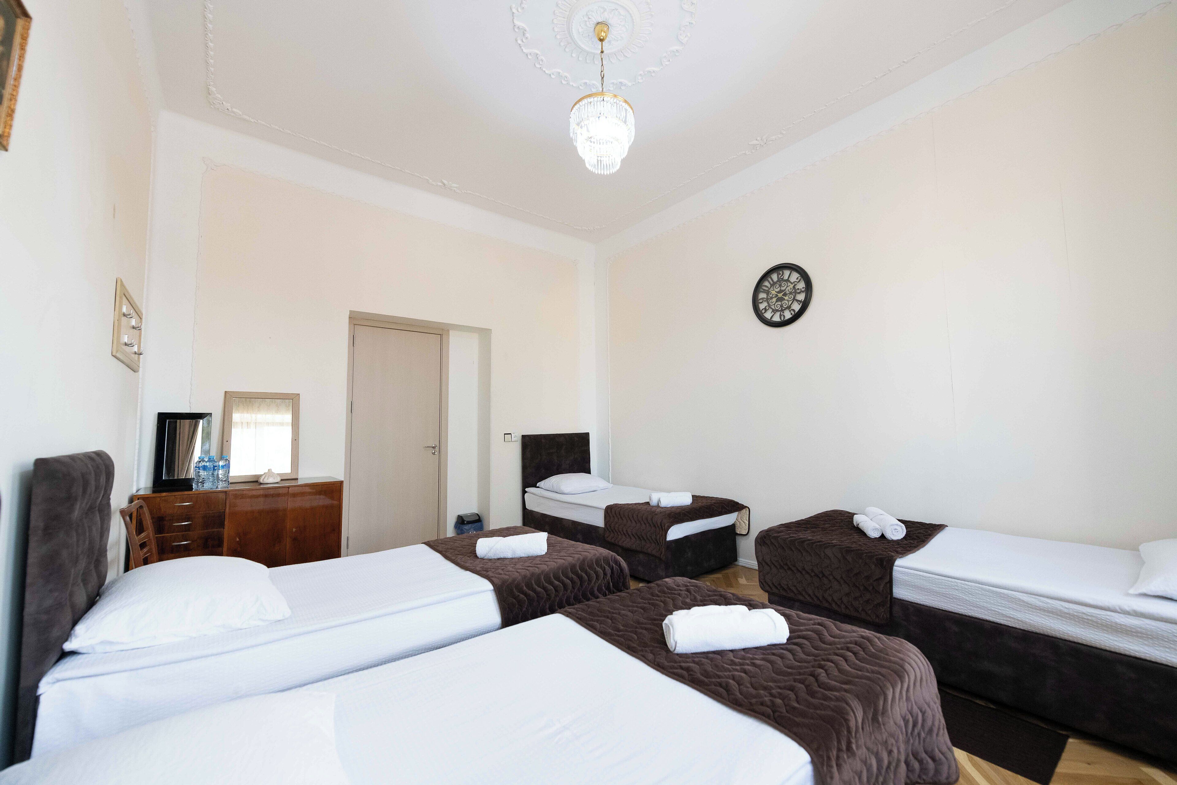 A hotel room with four beds, a wooden dresser, a mirror, and a chandelier.