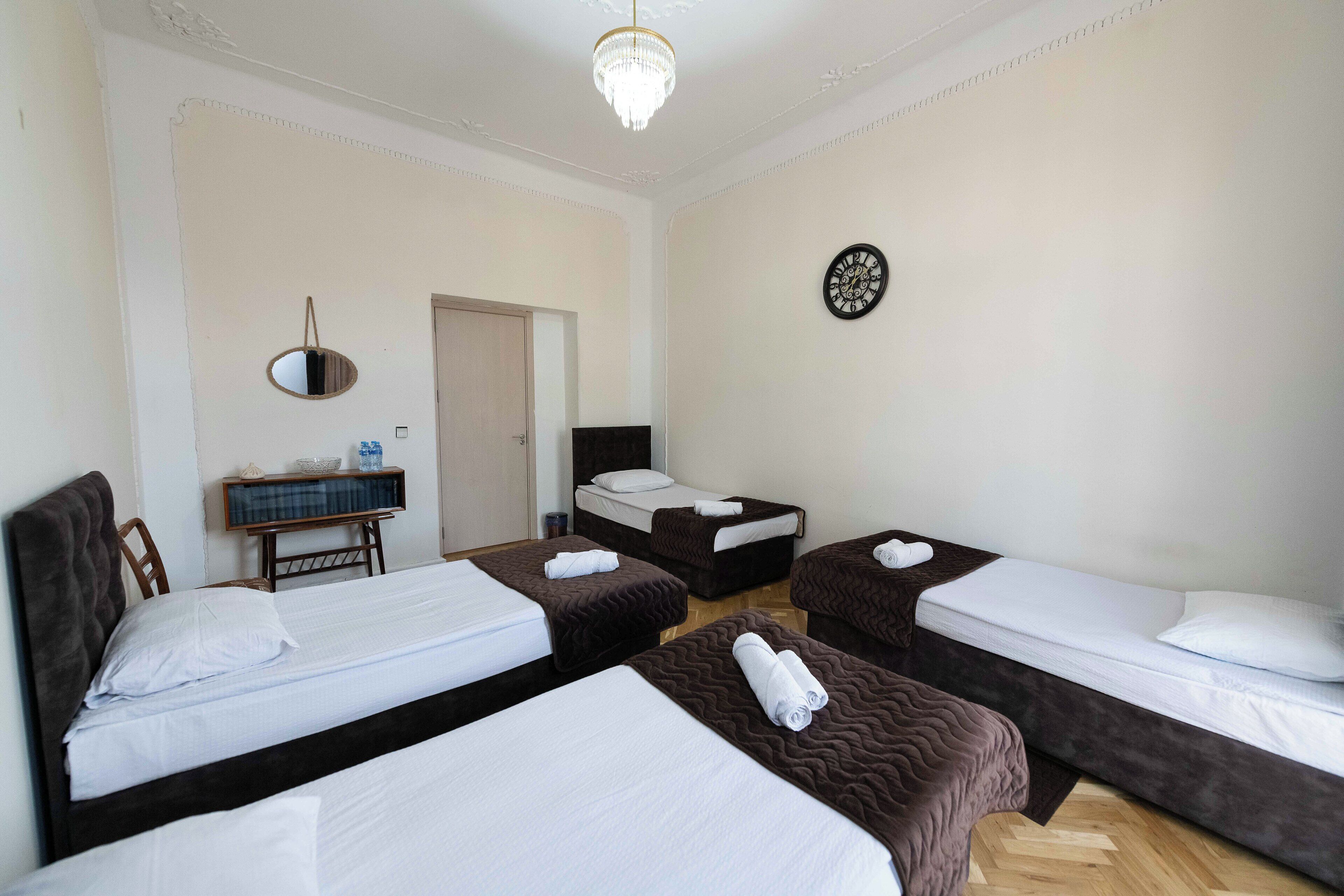 A hotel room with four beds, a chandelier, a clock, and a small table with a mirror and a bowl.