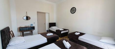 A hotel room with four beds, a chandelier, a clock, and a small table with a mirror and a bowl.