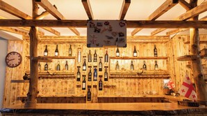 Una barra de madera con estantes llenos de botellas y vasos, un reloj y un cartel con varios artículos.