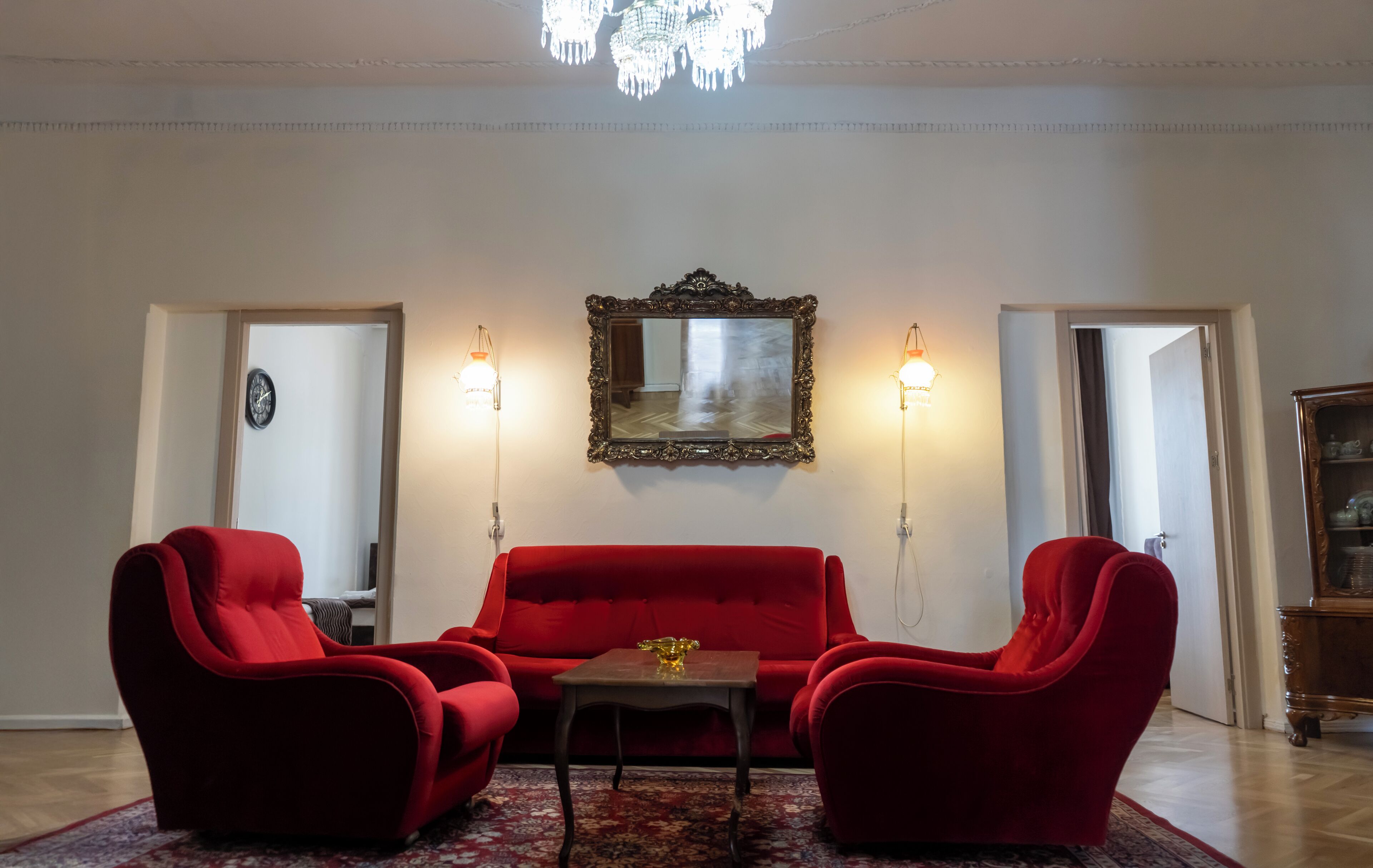 Una sala de estar con un sofá rojo, dos sillones, una mesita y una araña.