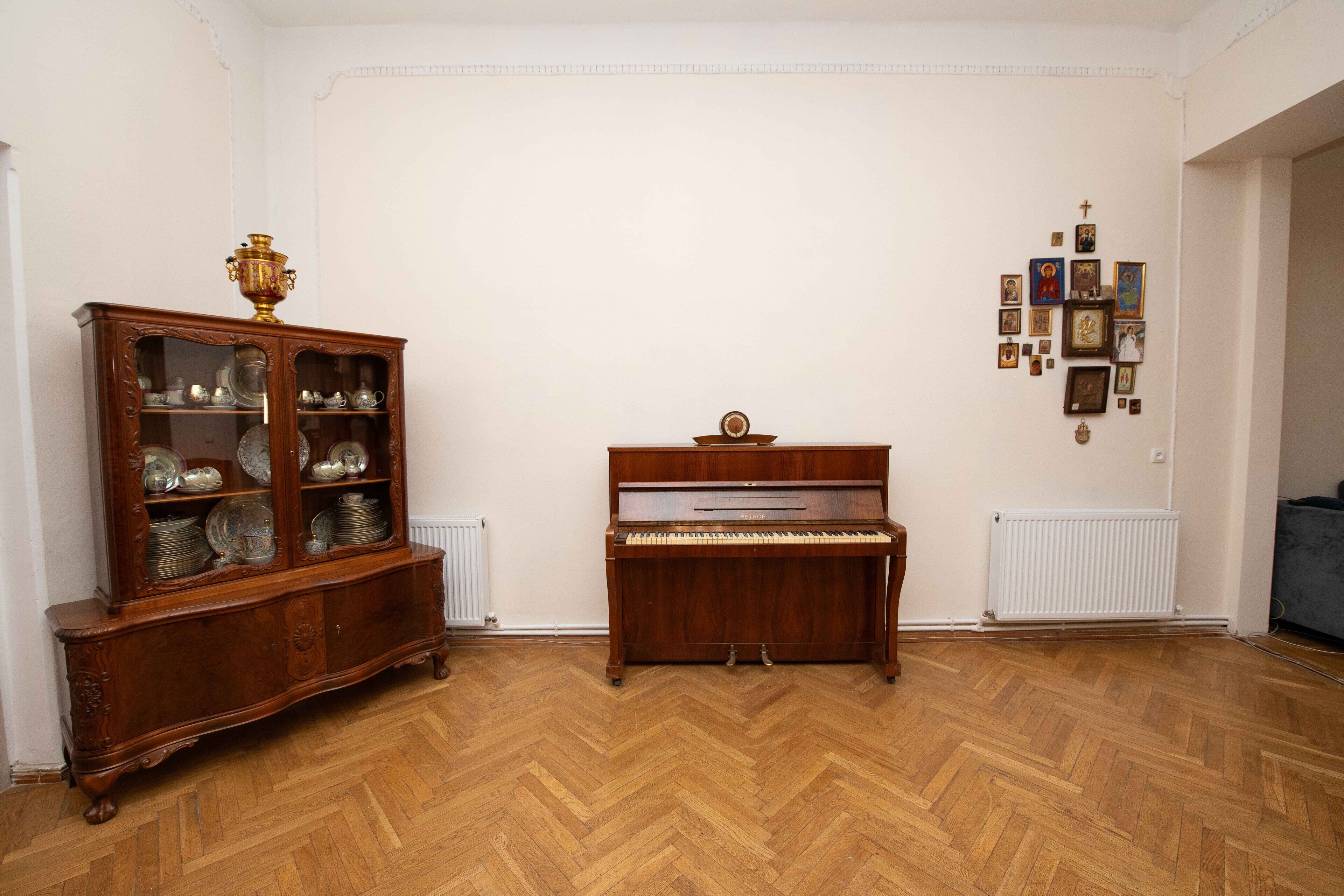A room with a wooden floor, a piano, and a china cabinet.