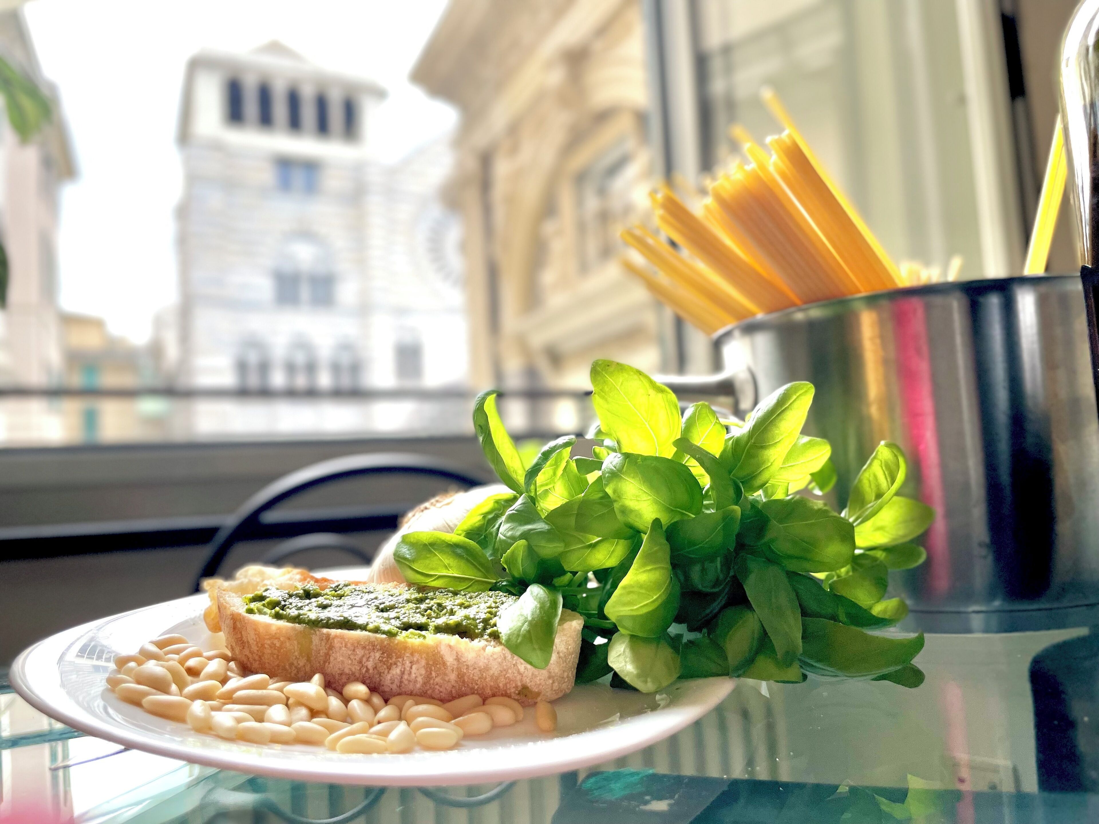 A plate with a sandwich, beans, and basil leaves on a glass table with a metal pot containing pasta in the background.
