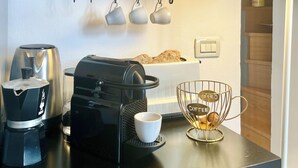 A kitchen counter with coffee-making equipment, a shelf with teapots and cups, and a wall decoration with a coffee theme. - Happy Family Apartments Cathedral (Genoa)