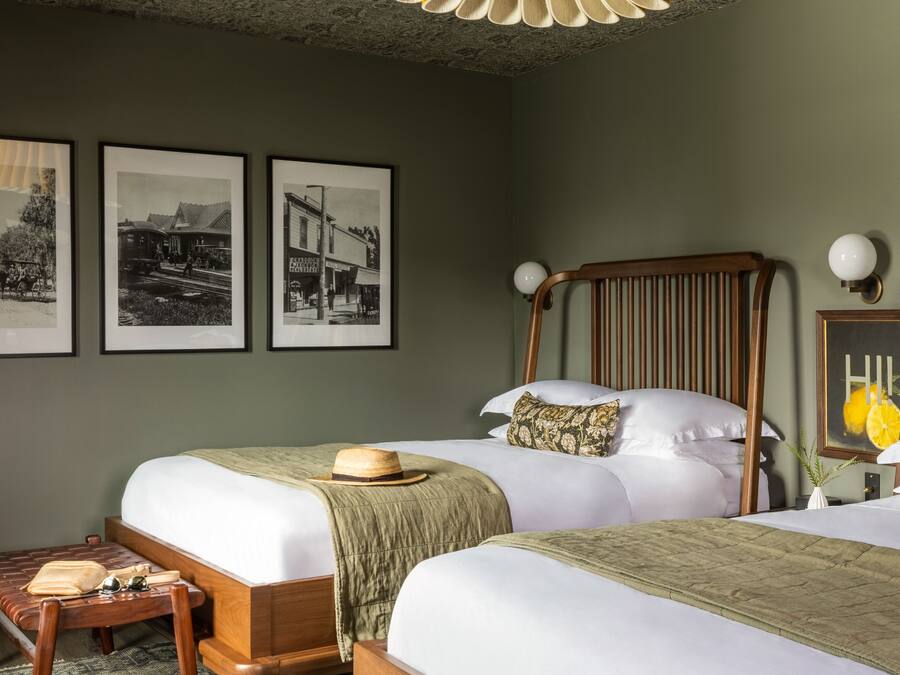 A hotel room with two beds, a wooden bench, a small table, and a ceiling light fixture.