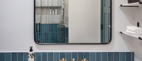 Une salle de bain avec un lavabo blanc, des robinets dorés, un miroir et une douche.