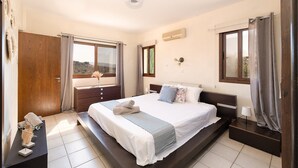 A bedroom with a large bed, a wooden wardrobe, a bedside table, and a window with curtains. - Villa Louna, Letymbou -  a private villa that sleeps 8 guests in 4 bedrooms (Letymbou)