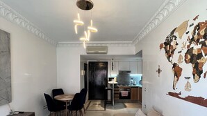A modern living room with a wooden coffee table, a beige sofa, and a dining area with a black table and chairs. There is a kitchen in the background with a world map on the wall. - Great Apartment Marrakesh Gueliz (Marrakesh)