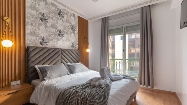 A neatly made bed with a striped blanket, a wooden nightstand, and a wall-mounted light fixture. - Great Apartment Marrakesh Gueliz (Marrakesh)