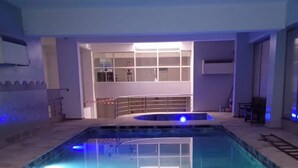 An indoor swimming pool with clear water, surrounded by a tiled floor and walls. There is a seating area with chairs and a table near the pool, and a staircase leading to an upper level with a balcony. - Great Apartment Marrakesh Gueliz (Marrakesh)