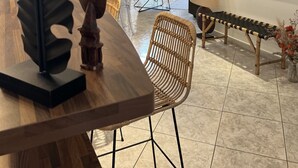 A modern living room with a wooden dining table, a large abstract painting, a wicker chair, and a bench. - Villa Sete les Pieds Dans Leau (Sète)