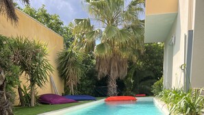 A pool area with a blue towel, a pair of slippers, and colorful cushions. - Villa Sete les Pieds Dans Leau (Sète)