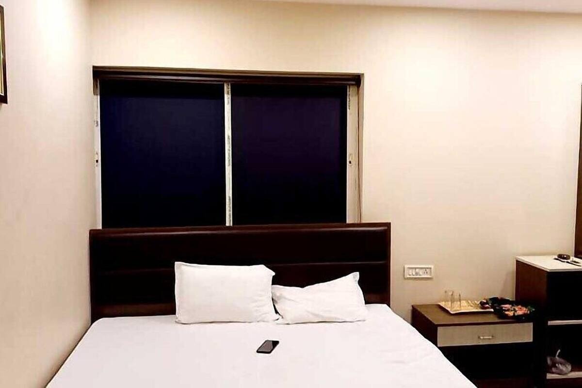 A hotel room with a bed, a nightstand, and a window with blinds.