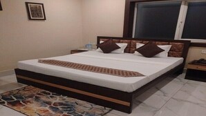 A bedroom with a large bed, a nightstand, a bedside table, a window, and a wall-mounted TV. - Hotel HMS Palace (Golmuri)