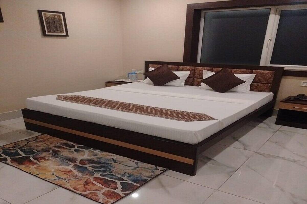 A bedroom with a large bed, a nightstand, a bedside table, a window, and a wall-mounted TV.