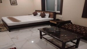 A compact hotel room with a single bed, a small sofa, a glass-top table, and a window. - Hotel HMS Palace (Golmuri)