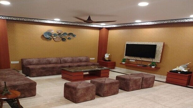 A living room with a sofa, ottomans, a coffee table, and a flat-screen TV mounted on the wall. - Hotel HMS Palace (Golmuri)