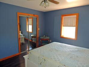 A bedroom with a bed, a desk, a chair, a window with blinds, and a ceiling fan.