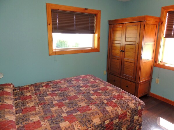 A bedroom with a bed, a window with blinds, and a wooden wardrobe.
