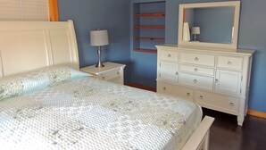 Een slaapkamer met een bed, nachtkastje, kaptafel en spiegel.