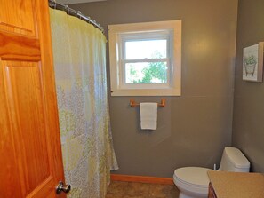 A bathroom with a wooden door, a shower curtain, a window, a towel rack, and a toilet.