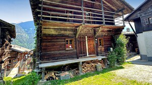 Un bâtiment rustique en bois, doté d’un balcon, d’un escalier en bois et d’une pile de bois de chauffage devant l’entrée.
