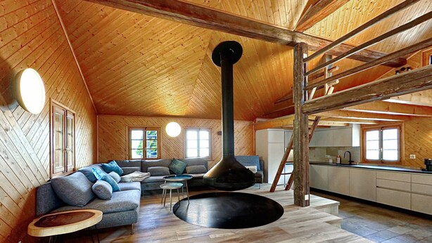 Un loft spacieux avec de hauts plafonds, une grande cheminée, un coin salon confortable et une cuisine dotée de meubles en bois.