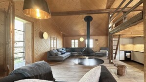 Un salon spacieux avec un grand canapé, une table basse et une cheminée. On aperçoit également un coin cuisine avec un réfrigérateur et un évier.
