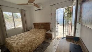 Un dormitorio con cama, escritorio, laptop y ventilador de techo, y vistas al exterior.