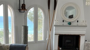 Una sala de estar con chimenea, un sofá, una mesita de centro y vistas al océano a través de amplios ventanales.