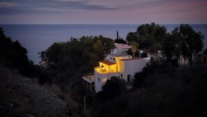 Una propiedad costera con un edificio destacado que tiene un balcón y una terraza, rodeada de árboles y vistas al mar.