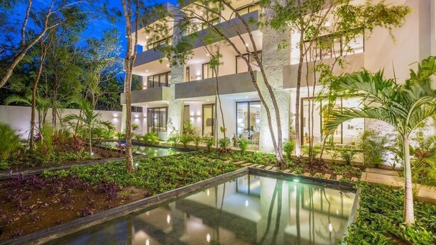 Um hotel moderno com piscina, rodeado por vegetação exuberante e árvores.