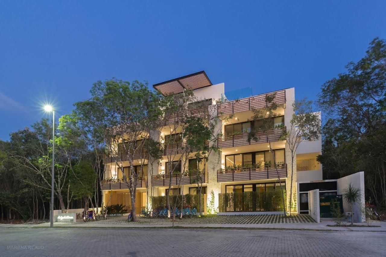 Un bâtiment moderne doté de nombreux balcons, de grandes fenêtres et d’un espace d’entrée pavé.