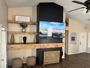 Cozy living space with a large flat-screen TV, fireplace, and decorative mantelpiece.