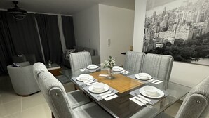 En moderne spisesal med et bord med glasplade, grå polstrede stole og et bybillede-maleri på væggen.